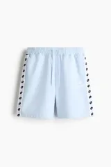 Short de felpa celeste de corte regular fit, con cintura elástica y cordón ajustable. Cuenta con bandas laterales blancas con el logo de Lotto repetido, bolsillos laterales y el logo de la marca bordado en una pierna.