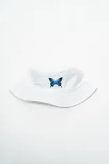 Gorro tipo bucket blanco con un bordado de una mariposa azul en el frente.