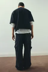 Pantalón cargo negro con efecto lavado, confeccionado en sarga de algodón suave. Presenta cintura elástica con cordón ajustable, cierre de botón a presión, bolsillos laterales, bolsillos cargo con solapa en las piernas y cordón ajustable en el bajo. Corte holgado.