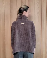 Polera de tejido suave con textura acanalada, cuello alto tipo tortuga, mangas largas y corte holgado con aberturas laterales en el ruedo.