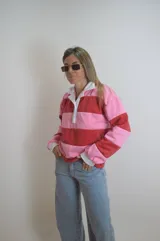 Sweater estilo rugby a rayas horizontales rosas y rojas con cuello blanco y cierre parcial con botones.