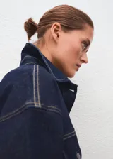 Chaqueta estilo tejano vaquero de algodón con elasticidad, color azul marino. Cuenta con cuello camisero, cierre frontal con botones, dos bolsillos de parche con solapa y botón en el pecho, mangas largas con puños abotonados y tira ajustable en la parte posterior.