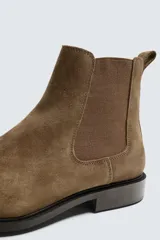 Bota estilo Chelsea de piel con acabado serraje color marrón claro, con elásticos laterales para facilitar el calce. Tiene horma redonda y suela con ligero tacón.