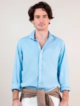 Camisa lisa de hombre color celeste, confeccionada en 100% algodón con acabado vintage. Presenta corte regular fit, cuello italiano, cierre con botones, manga larga con puño simple y logo bordado en el pecho.
