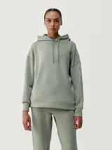 Buzo con capucha color verde, de tejido técnico, diseño holgado, hombro caído y bolsillos.