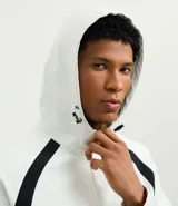 Campera deportiva con capucha, color blanco con recortes laterales en negro. Cuenta con cierre frontal, bolsillos funcionales y ajuste en la cintura.
