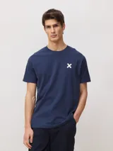 Camiseta de corte regular fit color azul marino, de manga corta y cuello redondo, confeccionada en 100% algodón orgánico, con un pequeño estampado de una cruz blanca en el pecho.