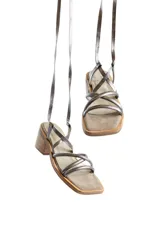 Sandalias de tacón bajo color bronce, con tiras finas cruzadas en el empeine y tiras largas para atar al tobillo. Tienen punta cuadrada y tacón de madera.