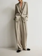 Blazer de corte recto confeccionado en viscosa, color gris topo. Presenta solapas clásicas, cierre frontal de dos botones y mangas largas con botones en los puños. Destaca por su diseño con detalles de efecto pintura en solapas, costuras y bolsillos. Incluye un bolsillo con solapa en el frente y abertura en la espalda.