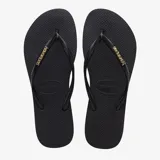 Ojotas Havaianas modelo Slim Logo Metallic, color negro, con tiras finas y logo metálico dorado. La suela es delgada y presenta textura antideslizante.
