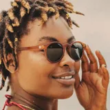 Lentes de sol Sunski modelo Dipsea, con armazón marrón translúcido de forma redonda y lentes polarizadas color verde oscuro.