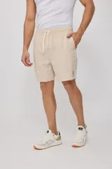Bermuda de corte recto en color beige, confeccionada en una mezcla de algodón, lino y poliéster. Presenta cintura elástica con cordón ajustable, bolsillos laterales y una pequeña etiqueta decorativa en el ruedo.