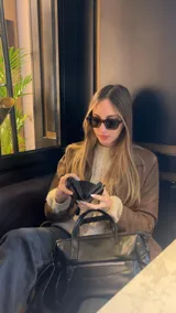 Cartera de mano y hombro color beige, de material símil cuero, con forma estructurada y redondeada. Posee dos asas cortas superiores y una correa larga ajustable y desmontable. Cuenta con un bolsillo exterior con cierre en la parte frontal.