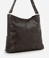 Cartera estilo hobo de cuero sintético en color gris oscuro, con diseño de media luna y correa fija para el hombro. Cuenta con bolsillos frontales funcionales, detalles de ojalillos metálicos plateados y un cordón cruzado ajustable con lazo en el centro.