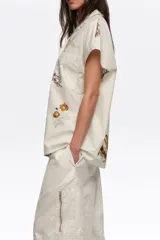 Camisa de manga corta color blanco con cuello solapa y estampado de temática marina con peces y estrellas de mar, con cierre frontal de botones y un bolsillo en el pecho.