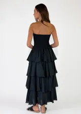 Vestido largo color crudo, sin tirantes, con cuerpo fruncido elástico tipo nido de abeja y falda de capas con volados con bordes deshilachados.