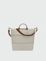 Bolso de viaje Longchamp modelo Le Pliage Original, de diseño ampliable, confeccionado en nylon negro con detalles en cuero marrón en las asas y solapa frontal con cierre de botón a presión. Incluye correa ajustable y extraíble.