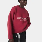 Suéter de punto grueso color bordó con diseño de cuello redondo y mangas largas. Presenta el logo de la marca Eme Studios tejido en técnica jacquard en el frente en color crema.