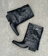 Bota corta de cuero negro con caña arrugada, puntera fina y hebilla decorativa en el lateral.