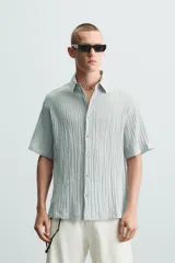 Camisa de manga corta con cuello solapa, confeccionada en tejido de mezcla de lyocell con textura de efecto arrugado y cierre frontal de botones.