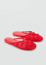 Zapato tipo mule destalonado de color rojo, confeccionado en tejido de malla con diseño de rejilla y adornado con abalorios decorativos en la parte superior. Presenta punta redonda y suela plana.