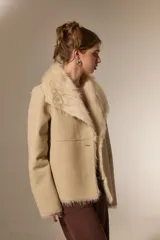 Chaqueta de eco-cuero color beige con interior y cuello de piel sintética al tono. Presenta un diseño holgado, cierre frontal con un botón y solapas amplias.