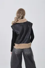 Chaleco sin mangas de cuero sintético negro con interior y detalles de piel sintética en color beige. Presenta cierre frontal asimétrico, cuello solapa y correas ajustables en la cintura.