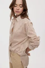 Camisa de rayas de calce relajado, confeccionada en tejido liviano y semitransparente, con cuello clásico, cierre frontal con botones, mangas largas con puños y hombros caídos.