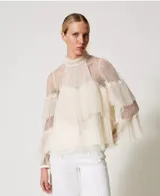 Blusa de tul point d'esprit color marfil, con cuello alto, volantes plisados, inserciones de encaje, mangas largas con puño y botón, cierre de lágrima con botón y placa con el logotipo Oval T en la parte trasera. Incluye top a juego antitransparencia y corte holgado.