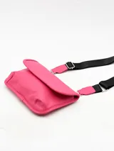 Bolso pequeño tipo bandolera o cartera de mano, color fucsia vibrante, con solapa frontal y correa ajustable de tela negra con herrajes metálicos.