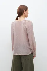 Blusa color beige con textura de lunares en relieve, escote en V y mangas largas con puños elásticos.