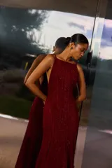 Vestido largo color burdeos con brillos, escote halter y espalda descubierta. El diseño es ajustado hasta la rodilla y se abre en una falda acampanada con vuelo.