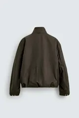 Cazadora de corte cropped confeccionada en algodón con acabado encerado. Presenta cuello subido, cierre frontal con cremallera oculta por solapa con botones a presión, bolsillos de plastrón con solapa en el delantero y bajo ajustable con elástico interior.
