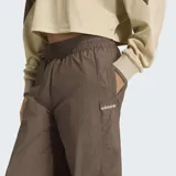Pantalón deportivo Adidas de corte holgado, color marrón con detalles en beige en la parte inferior de las piernas. Presenta cintura elástica con cordón de ajuste y logo de la marca bordado en el muslo.