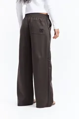 Pantalón de corte ancho y relajado en color marrón, con cintura elástica, bolsillos laterales y costuras verticales decorativas en contraste a lo largo de las piernas.