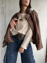 Remera de lanilla color beige, de corte holgado y manga larga. Presenta una hilera de botones decorativos a lo largo de toda la parte externa de las mangas.