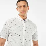 Camisa blanca de corte recto y manga corta, con estampado de palmeras, estrellas y lunas en color negro.