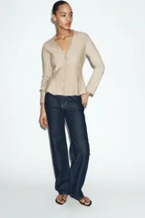 Chaqueta entallada de punto con escote en pico y manga larga. Presenta un diseño con bajo en evasé tipo peplum y cierre frontal con botones forrados a tono.