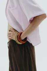 Pack de cuatro pulseras rígidas de madera recubiertas con rafia tejida en tonos rosados, naranjas y verde oliva.