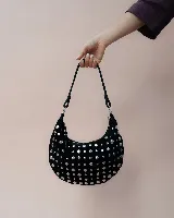 Bolso de mano tipo hobo, confeccionado en gamuza color marrón oscuro, decorado con tachas metálicas circulares en toda su superficie. Cuenta con un asa corta integrada y un diseño curvo distintivo.
