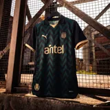 Camiseta de fútbol Puma del Club Atlético Peñarol, modelo Third Jersey 2026. Diseño en tonos oscuros con patrón de ondas en relieve, detalles en color dorado en cuello, mangas y logos. Incluye escudo del club, logo de Puma y sponsor Antel en el frente.