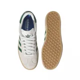 Championes Adidas modelo Gazelle ADV, con diseño clásico de perfil bajo. Presentan una capellada de gamuza en color beige claro, con las icónicas tres tiras laterales y refuerzo en el talón en color verde oscuro. Incluyen cordones blancos, suela de goma color caramelo y el nombre del modelo estampado en dorado en el lateral.