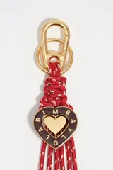 Llavero con mosquetón dorado, cuerpo de cuerdas entrelazadas rojas con detalles blancos, y dije central en forma de corazón esmaltado en color marrón con letras doradas y un corazón metálico dorado en el centro.