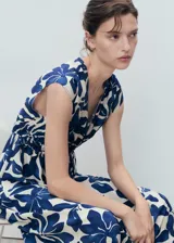 Vestido largo de corte evasé con estampado botánico en azul sobre fondo crudo. Presenta cuello de pico, mangas cortas y un panel fruncido en la cintura con cordón ajustable.