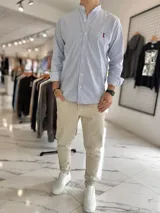 Camisa de manga larga con cuello mao, a rayas verticales celestes y blancas, con pequeño bordado en el pecho.
