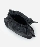 Cartera tipo shoulder bag de tamaño grande, confeccionada en poliuretano con acabado que imita el cuero. Presenta un diseño desestructurado con solapa superior, cierre mediante cordón de ajuste y detalles metálicos plateados en el frente. Incluye correa ajustable para llevar al hombro o cruzada.