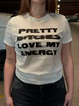 Remera blanca de manga corta, corte al cuerpo, con estampa frontal en negro con la leyenda "Pretty Bitches Love My Energy".