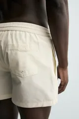 Short de baño de color beige con textura seersucker, cintura elástica con cordón ajustable, bolsillos laterales y forro interior.
