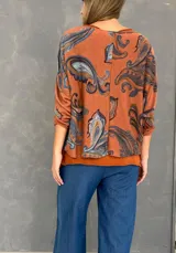 Blusa de algodón con diseño de doble capa, compuesta por una musculosa base y una capa superior de tejido liviano con estampado paisley en tonos naranja, celeste y marrón. Presenta un corte oversize y mangas tres cuartos.