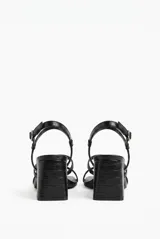Sandalias de tacón medio y cuadrado, color negro con textura efecto cocodrilo, tiras finas cruzadas en el empeine y tira ajustable con hebilla en el tobillo.
